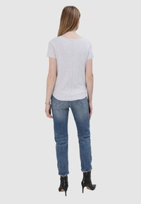 Szara bluzka z krótkim rękawem o okrągłym dekolcie, z centralnym szwem. W połączeniu z niebieskimi dżinsami i czarnymi botkami na wysokim obcasie.