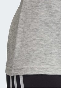 Gros plan sur l'ourlet d'une chemise en tissu grisé clair mélangé, portée sur un pantalon noir avec trois bandes verticales grises claires.