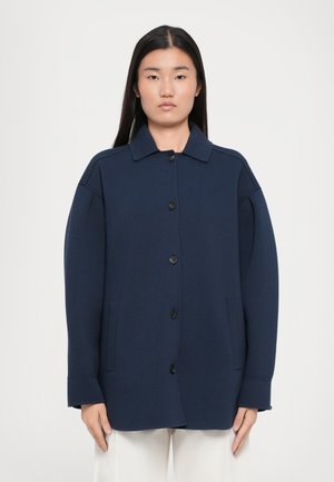 Navy blue oversized jacket with a collar, front buttons, and side pockets; made of soft fabric with a smooth texture.