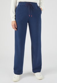 Marineblauwe joggingbroek met een gestructureerde afwerking, voorzien van een elastische tailleband, trekkoord en zijzakken, gecombineerd met witte sneakers.