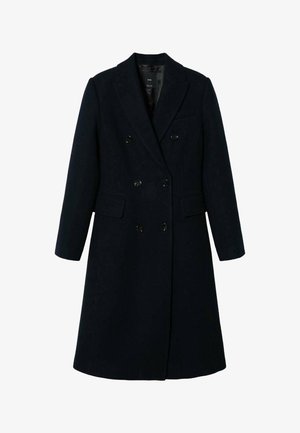 Manteau en laine noir à double boutonnage avec revers crantés, deux poches à rabat et boutons noirs, porté sur un haut foncé à col montant.