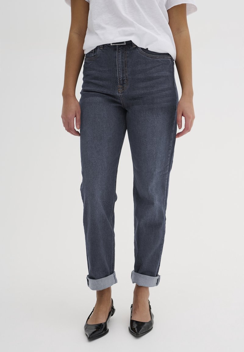 Jeans in denim blu scuro con vita alta, gamba dritta e orli cuffed, arricchiti da dettagli di cucitura sottili. Indossati con scarpe nere.