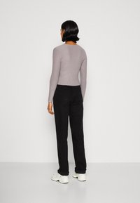 Grau geripptes Langarmoberteil kombiniert mit hochgeschnittenen schwarzen Hosen; das Modell trägt weiße Schuhe. Insgesamt eine figurbetonte Silhouette und glatte Textur.