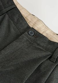 Tmavě šedé kalhoty na míru s předními sklady, černým zapínáním na knoflík a béžovým podšitím pasu.