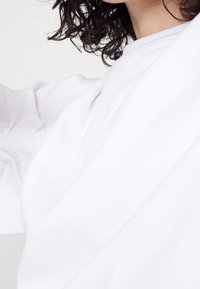 Vit sweatshirt med avslappnad passform, rynkade ärmar och textil med struktur. Synliga design detaljer inkluderar sömmar och rundad halsringning.