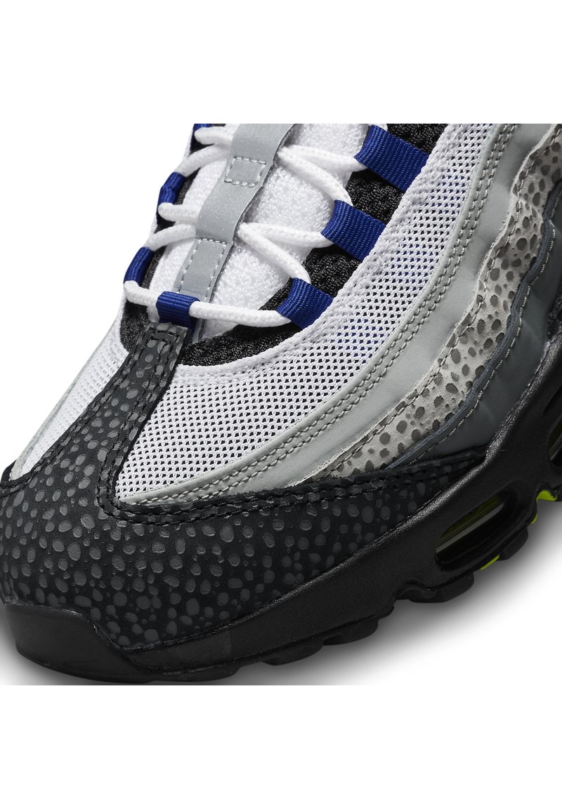 Zapatillas Nike con parte superior de malla en tonos gris, negro y azul. Suela de goma negra texturizada con pequeños patrones circulares. Diseño con cordones.