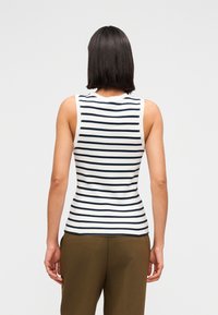 Αμάνικη ριγέ μπλούζα σε λευκό με ναυτικό μπλε ρίγες· εφαρμοστή γραμμή με στρογγυλή λαιμόκοψη. Το μοντέλο φοράει παντελόνι σε χακί χρώμα, ο δεσμός παρουσιάζεται από πίσω.