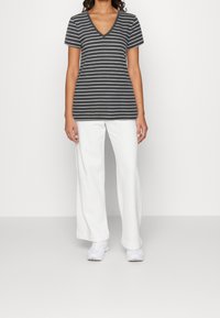 Camiseta de v-neck a rayas en gris y blanco combinada con pantalones blancos holgados y zapatillas blancas, con mangas cortas y un corte relajado.