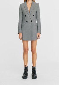 Robe blazer à double boutonnage gris rayé avec boutons noirs, col à revers et poches avant. Associée à des bottes de combat noires à lacets.