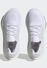 Witte hardloopschoenen met een ademend mesh-bovenwerk, platte veters en gewatteerde zolen. Bevat "End Plastic Waste" branding.