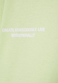 Texte blanc sur tissu vert clair indiquant "Create consciously. Live intentionally."