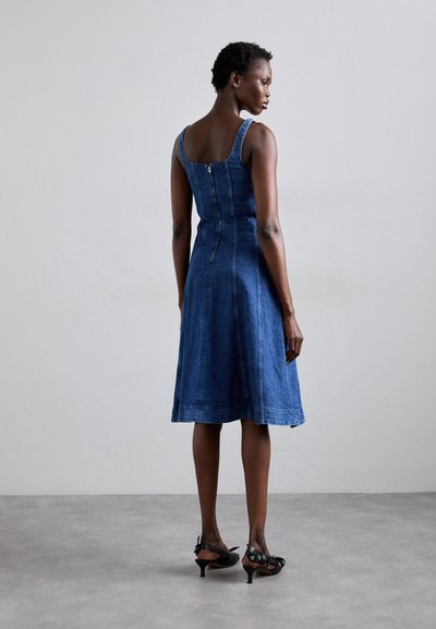 Denim jurk met een aangesloten lijfje, uitlopende rok en schouderbanden. De achterkant heeft een verticale rits. Gepaard met zwarte hoge hakken sandalen.