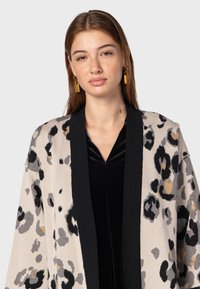 Beige cardigan met zwart en grijs luipaardprint, wijde mouwen en een solide zwarte rand. Gecombineerd met een zwarte v-hals top.