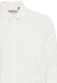 Weißes Langarmshirt aus leichtem Stoff, mit durchgehender Knopfleiste, spitzem Kragen und einer aufgesetzten Tasche auf der linken Seite.