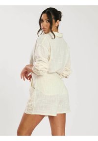 Vestido camisero de lino color beige claro con un ajuste relajado, mangas largas arrolladas, bolsillos laterales y costuras decorativas a lo largo del dobladillo.