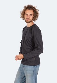 Langärmliges schwarzes T-Shirt aus weichem Baumwollmix, mit runden Halsausschnitt und seitlichen Nahtdetails. Getragen mit hellblauen Denim-Jeans.