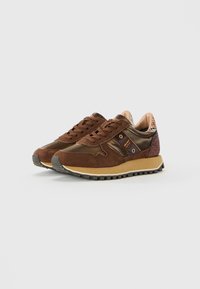 Sneakers en daim et cuir marron avec des semelles beiges et des accents de talon à motifs, vue de côté en angle sur un fond blanc.