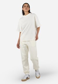 Oversized cream t-shirt with short sleeves, paired with cream sweatpants; both made of soft fabric. Details include logo embroidery.