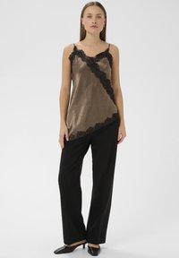 Brun satin camisole med sort blonderkant, der har et diagonalt design, båret med sorte vidde-bukser og spidse mule-sko.