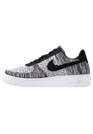 Low-top Nike sneaker med sort og hvid strikket overdel, sort swoosh-logo, sorte snørebånd og hvid sål med Air-dæmpning.