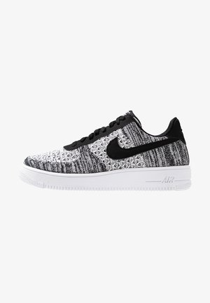Niskie buty sportowe Nike z czarno-białą dzianą cholewką, czarnym logo Swoosh, czarnymi sznurowadłami i białą podeszwą z amortyzacją Air.