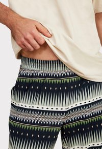 Musterhose mit marineblauem Grundton und geometrischen Designs in Grün, Creme und Beige. Gummibund und entspannte Passform.