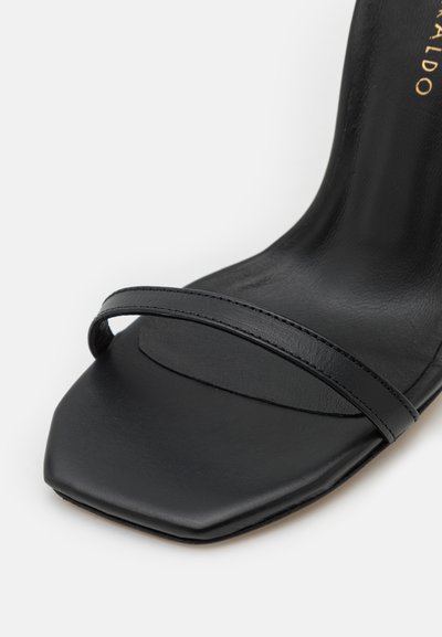 Sanda negra de tacón alto con diseño de punta cuadrada, suela elegante y una tira estrecha en la parte superior. Textura de cuero suave.