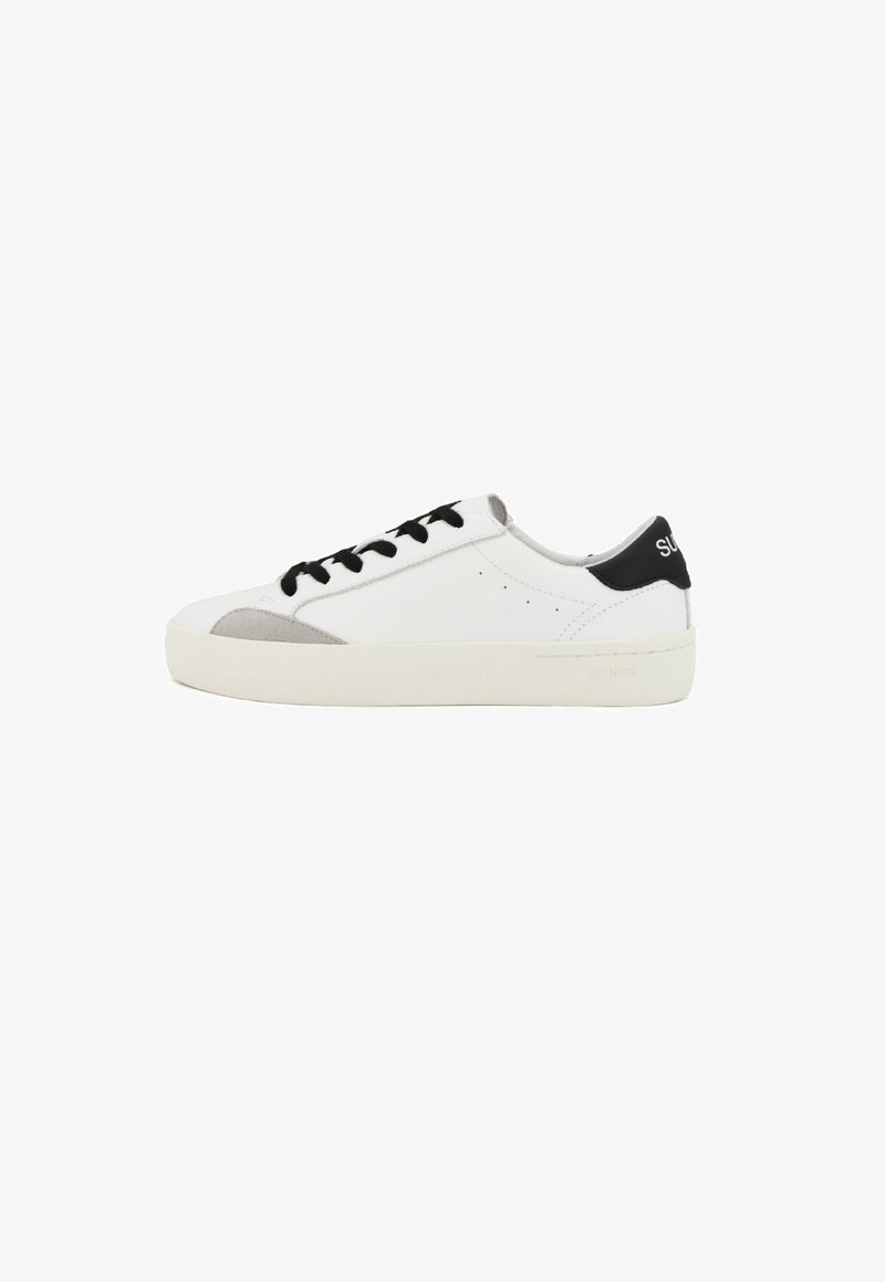 Zapatillas blancas con acentos negros, detalles de ante gris en la punta, agujetas planas negras y una suela de goma texturizada. Diseño minimalista.