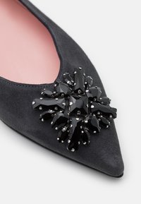 Chaussure plate pointue en daim noir avec un gros ensemble décoratif de gemmes noires facettées sur le bout et une doublure intérieure rose clair.