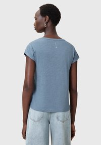 Blå kortærmet skjorte med rund halsudskæring og oprullede ærmer. Bagsiden har et lille trykdetalje. Kombineret med lyse denimjeans.