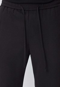 Pantalon de survêtement noir avec taille élastique, fermeture à cordon, tissu en coton lisse et coupe droite. Pas de motifs ni d'accents visibles.