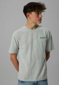 Lys grå bomulds t-shirt med korte ærmer, har en rund halsudskæring og et blåt "SPORTS DEPT." logo trykt på venstre brystområde.