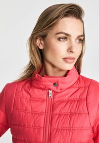 Różowa kurtka ocieplana z wysokim kołnierzem, zamkiem błyskawicznym i poziomymi szwami. Gładka faktura z metalowymi detalami zamka.