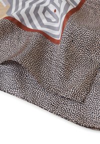 Foulard di seta con un motivo a macchie bianco e nero, caratterizzato da un design geometrico grigio e un bordo color ruggine. Tessuto morbido e testurizzato.