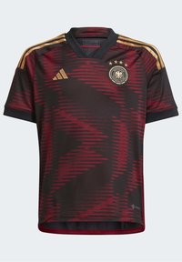 Saksan jalkapalloasu, tummanpunainen mustilla yksityiskohdilla, jossa on sahalaitakuviot, V-pääntie ja kultainen kolmen tähden emblem rinnassa.