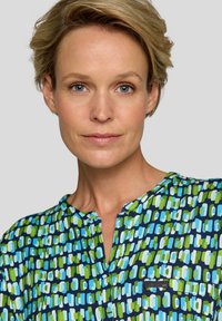 Mehrfarbige Bluse in Blau- und Grüntönen, mit einem geometrischen Muster, einem V-Ausschnitt und einem kleinen Taschendetail auf der Brust.