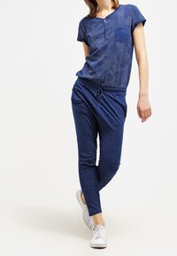 Modrý polo top s krátkým rukávem a kapsou, spárovaný s volnými jogger kalhotami. Texturovaná látka s elastickým pasem a manžetami na kotnících.