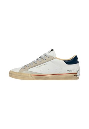 Sneaker bianca low-top con area delle stringhe in suede beige, linguetta del tallone blu navy, striscia rossa sulla suola in gomma sporca e testo laterale dorato "Céline London"