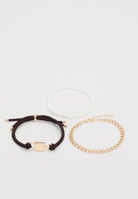Three bracelets: one with brown rope and gold hardware, a clear beaded one, and a gold chain link bracelet.