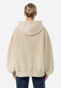 Felpa oversize beige con una texture morbida, cappuccio con coulisse e orlo a costine. Presenta spalle abbassate e una silhouette rilassata.