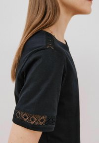 T-shirt nero a maniche corte con dettagli in pizzo sui polsini, una semplice scollatura rotonda e una texture di tessuto liscia e morbida.