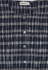 Navy and white checkered button-up shirt with textured fabric, featuring gathers along the seams and round plastic buttons.