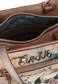 Sac à main synthétique marron avec un design graphique coloré, des accents métalliques et une sangle texturée. Comprend un compartiment principal zippé et une poche intérieure.