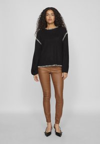 Čierny pletený sveter s bielym šitím pozdĺž okrajov, kombinovaný s hnedými nohavicami z umelého kože a čiernymi lodičkami s ostrou špicou.