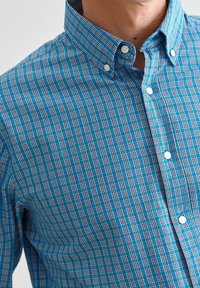 Camicia a quadri blu e nera con colletto, dotata di bottoni bianchi e un motivo di tessuto testurizzato.