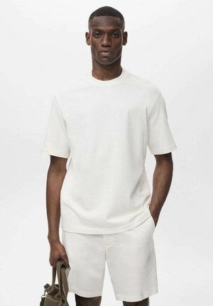 Witte katoenen t-shirt met korte mouwen, relaxte pasvorm, ronde halslijn, gedragen met bijpassende shorts en een groene tas. Soepele textuur.