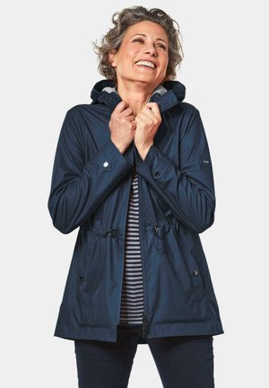 Veste étanche navy avec taille à cordon de serrage, fermeture éclair et capuche. Comprend des boutons-pression et une doublure intérieure rayée.