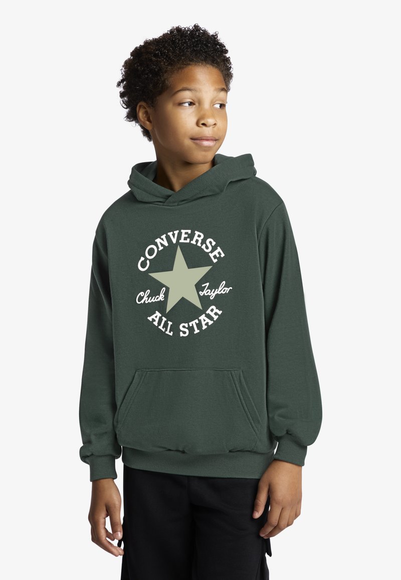 Žalias džemperis su gobtuvu, pagamintas iš minkšto medvilnės audinio, su kišene priekyje ir baltu žvaigždės logotipu bei „Converse All Star“ tekstu apskritimo forma.