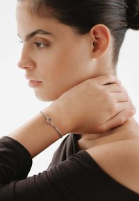 Pulsera de plata con un eslabón ovalado, que presenta un diseño de cadena texturizado. Se lleva en una muñeca, resaltando un aspecto sencillo y elegante.