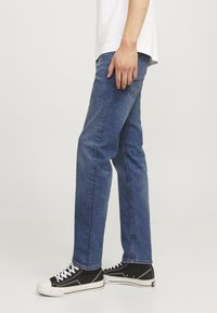 Jeans de denim azul de pierna recta con un lavado medio, combinados con zapatillas altas negras. Los jeans tienen un diseño clásico de cinco bolsillos.